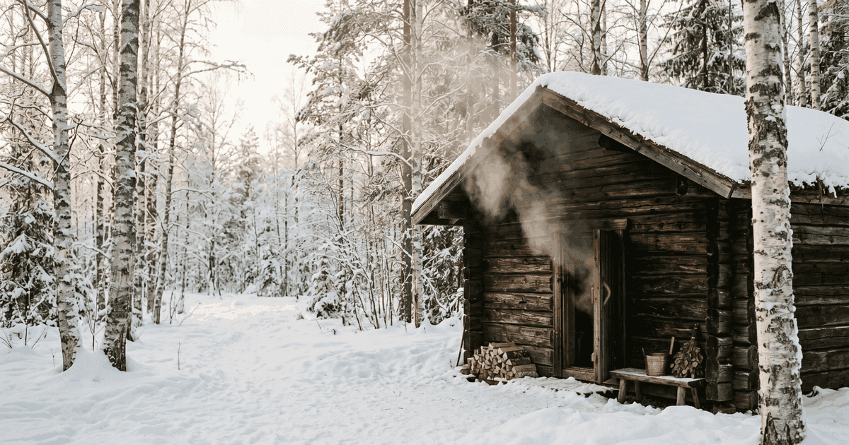 A chimneyless Finnish savusauna interior with blackened log walls and a smoldering stone pile beneath simple wooden benches